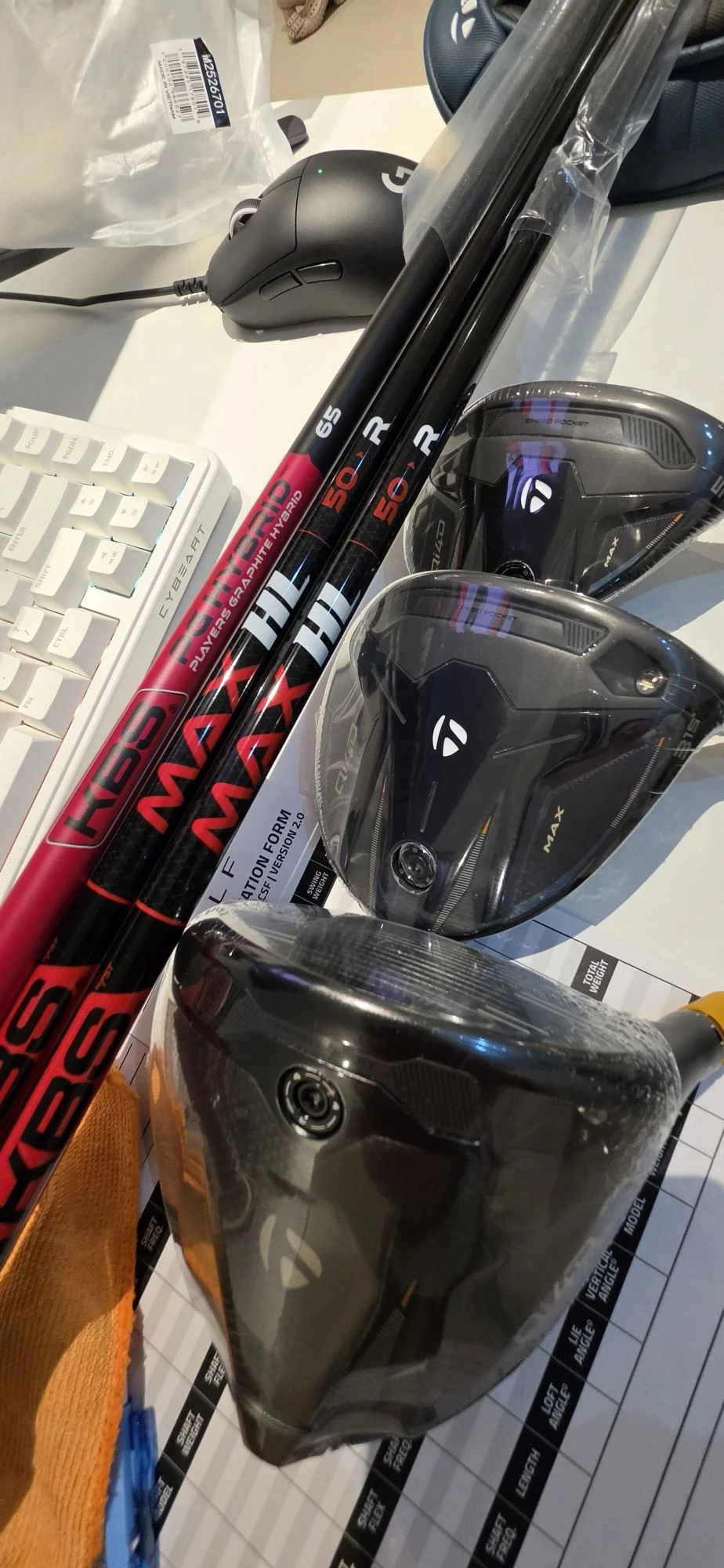 Golf clubheads and shafts prepared on the ASUBURE workbench beside a build specification form